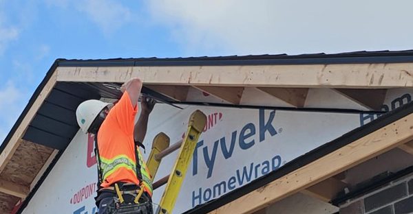 Image of an Aurora Exteriors Inc employee affixing black vented aluminum soffit material to a new construction home.