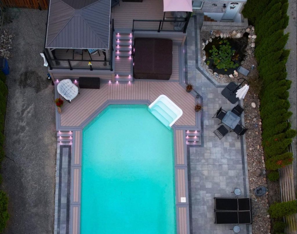 A Large Multilevel deck designed and constructed by Aurora Exteriors Inc from TruNorth Composite Decking. Featuring Gemstone Deck Lighting glowing purple on the decks 3 stairways and Powdered Aluminum Railings with Glass inserts overlooking the pool.