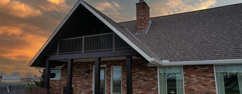 An image of a house at sunset after a Porch Renovation project was completed by Aurora Exteriors Inc to update the upper balcony with aluminum hand railings in commercial brown, and espresso wood grain column wraps were added to hide the unsightly rusting structural supports that were previously exposed.