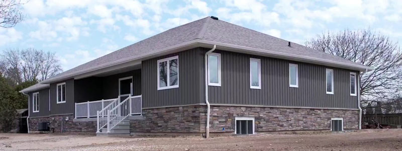 The front view of a custom built home finished by Exterior Finishing company Aurora Exteriors in a stunning vertical vinyl in a castlemore colour, versetta stone skirting in sterling and white aluminum railings on the front porch.