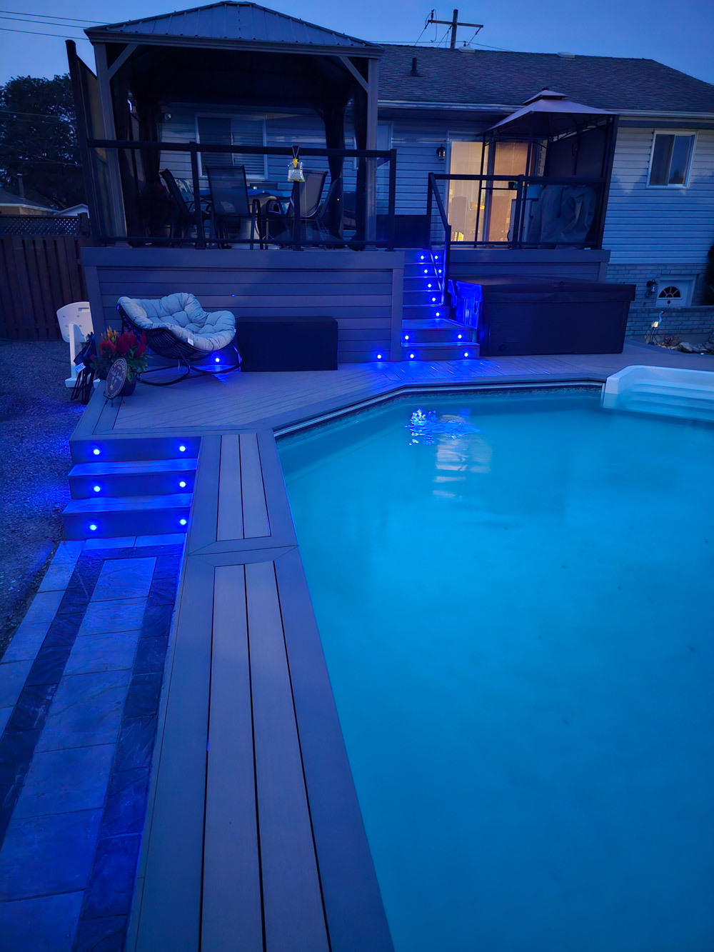 image of a custom composite deck with gemstone deck lighting, pictured at night with deck lights in a dark blue colour.