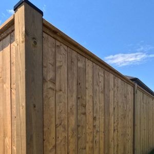 Outward facing side of pressure treated wood fence with black post caps installed by Aurora Exteriors Inc.