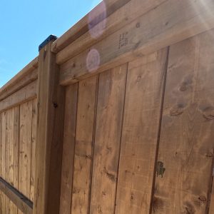 Backside or inside view or pressure treated vertical wood pivacy fence up close showing wood knot, texture and black post cap.